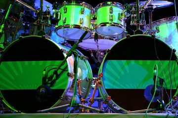 Double bass drum set with some tom-toms, microphones and stands. Green backlight.