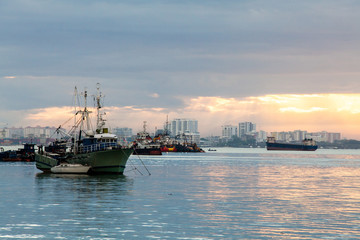 Fototapeta premium Sunrise by the shore with view of commercial and fishing boat