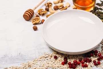 Cereal and various delicious ingredients around empty plate for breakfast on white background. Top view.