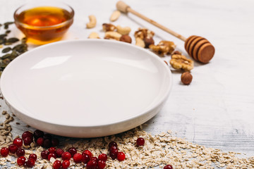 Cereal and various delicious ingredients around empty plate for breakfast on white background. Top view.