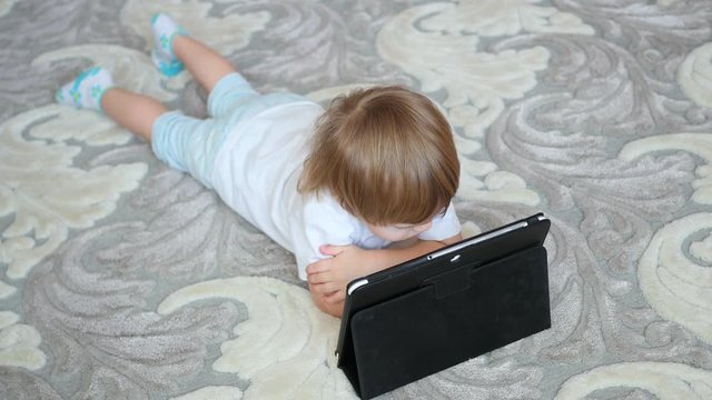 child looks cartoons on tablet pc on floor