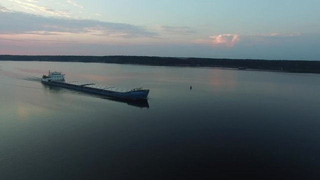 Cargo transport ship sailing on a wide river. Summer dawn. The camera moves in the air away from the barge. The island in the middle of the river.
