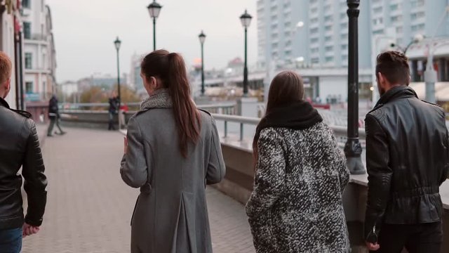 Two trendy girls and two stylish men cheerfully walk in the city and talk. Slow mo, steadicam shot, back view
