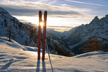 tra i due sci,si vede il tramonto del sole dietro le montagne del monte Bianco