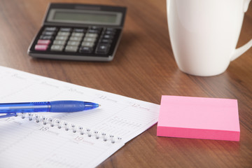 Workplace in office with calendar, pen, calculator, post it, cup