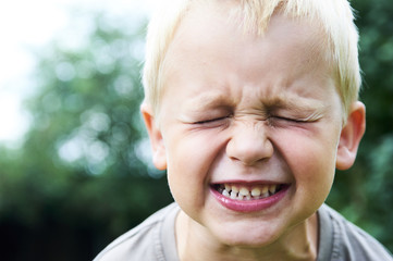 Portrait of a little child blond boy making faces. Outside with natural background. 