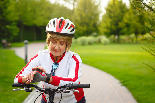Mature woman using smart watches on bike in the beautiful park. Healthy and active retirement concept