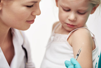 Little child having flu vaccine in hospital. Close-up of woman doctor hands in gloves holding...
