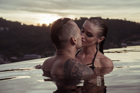 Romantic sensual couple alone in infinity swimming pool over beautiful tropical and sunset sky background