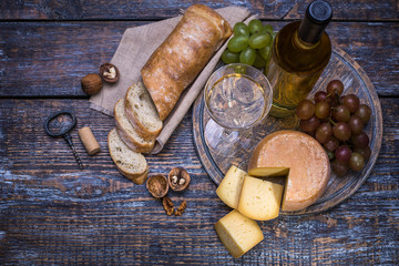 White wine in a bottle, cork, bottle screw and a set of products - cheese, grapes, nuts, olives, figs on a wooden board, background