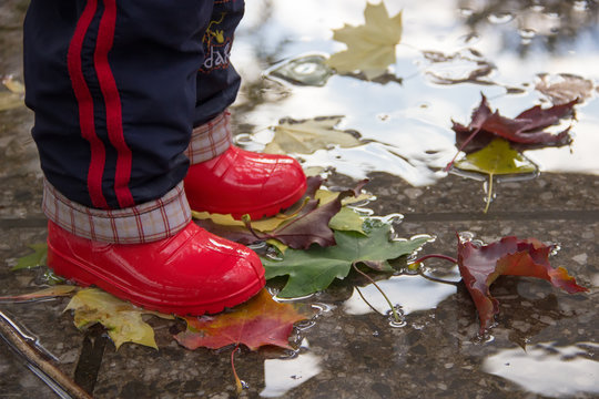 Children's legs in red rubber boots in a puddle.