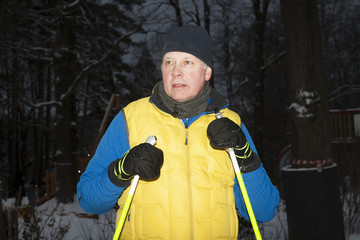 мужчина в лыжном костюме и с лыжжными палками в зимнем спортивном парке после пробежки