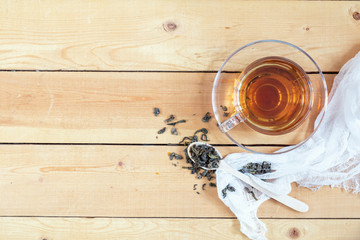 Cup of green hot tea and dry tea in wooden spoon on light wooden table, top view