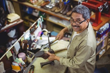 Fototapeta premium Portrait of smiling shoemaker hammering on a shoe