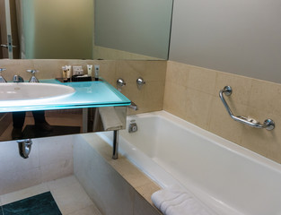 hotel bathroom with basic amenities,  bath tub, hand rail, sink,  lights, 
