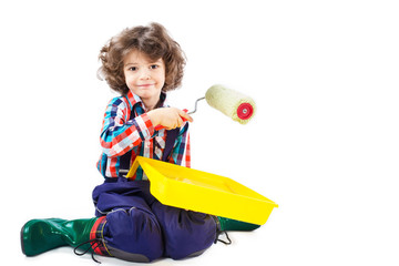 Little curly boy sitting on the floor in the pose of a hero, paints the wall roller and looking at the camera. White background.