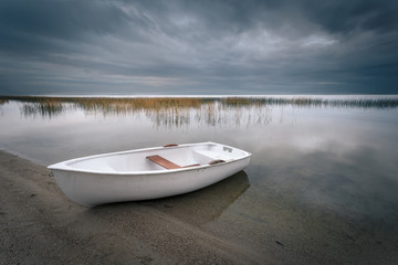 Autumnal cloudy landscape. A beautiful view at the Lake with a lonely white rowing boat parked on...