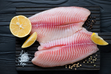 Close-up of raw tilapia fillet with sea salt, pepper and lemon