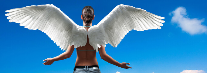 Girl with angel wings standing with spread arms against blue sky
