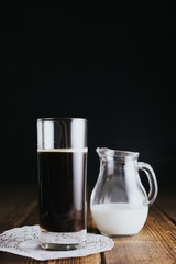 Jar of milk and glass of coffee against dark background