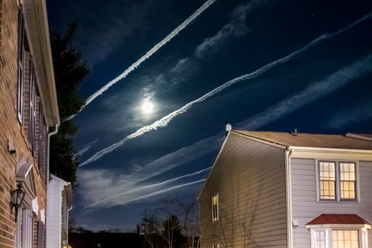 Bright full moon with night sky, airplane trails and homes