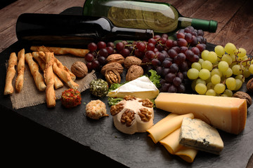 Assorted cheeses on round wooden board plate Camembert cheese, cheese grated bark of oak, hard cheese slices, walnuts, grapes, crackers, bread, thyme, dark black wood background