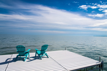 Obraz premium Muskoka or Adirondack Chairs on a dock overlooking the water with blue sky