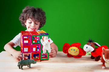 The beautiful smiling kid in a white t-shirt checks construction of the house. Friends together build the house. On a green background.