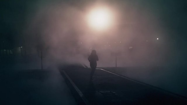 Silhouette of woman running through the mist  at night. Illuminated by night. Slow motion