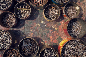 Nails and screws in rusty tin cans on wooden background