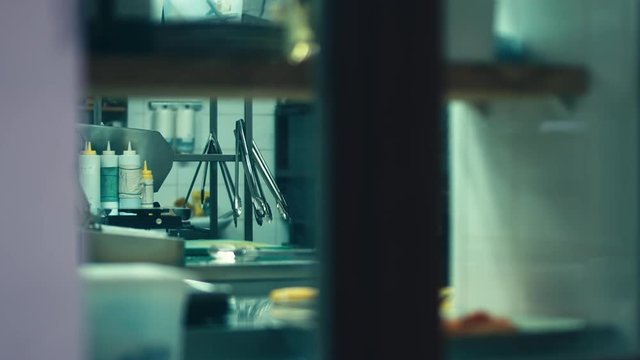 Unrecognizable chief walking around restaurant kitchen as seen through the window. HD 120 FPS SLO MO