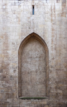 An empty door frame found in a stone wall of an old church. The arch is pointed, gothic style, with a marble pattern inside and stone blocks on the outside.