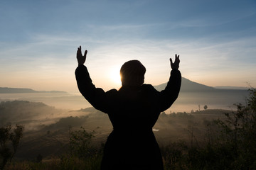 Silhouette tourist woman raised hand to sunrise and feeling happ