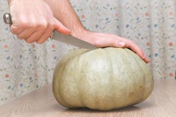 Hands cutting the pumpkin with knife on the wooden table in the kitchen. Healthy eating and lifestyle.