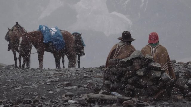Peruvian muleteers seated on the rocks during a snowfall near the Nevado Pastoruri . 
