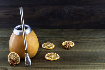 Yerba mate in gourd matero with bombila and dried lemon slices on wooden background.