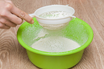 Hands with a sieve sift the flour into a bowl in the kitchen. Healthy eating and lifestyle.
