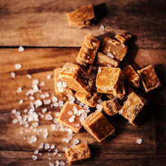 Golden Salted caramel pieces and sea salt macro on wooden board.