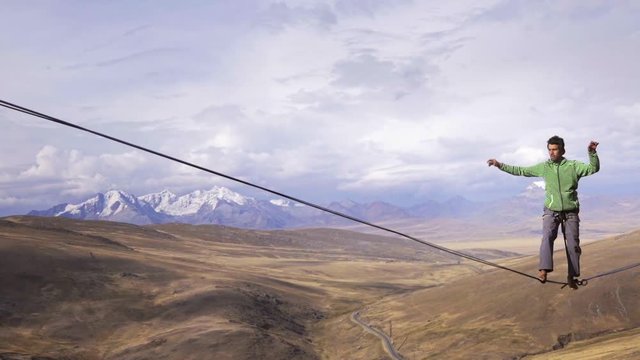 Slackliner balancing on tightrope between two rocks, Snowy mountains of the Huascaran park on the background, Peru. Slow motion