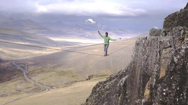 Slackliner balancing on tightrope between two rocks, Snowy mountains of the Huascaran park on the background, Peru. Slow motion
