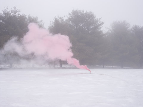Flare on grass, in snow covered park, emitting pink smoke