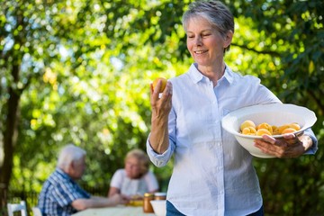 Senior woman holding a bowl of apricot in garden - Powered by Adobe