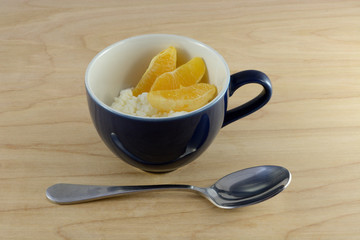 Cottage cheese and orange slices in blue uip with spoon on wooden table