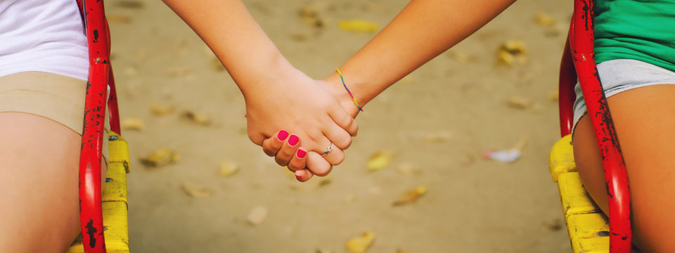 Two Teenage Girls Holding Hands While Sitting In Park