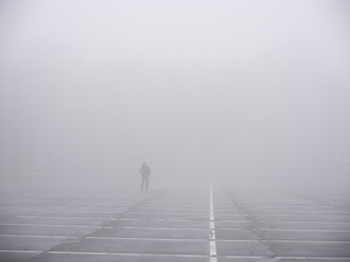 Person walking across empty car park, in mist