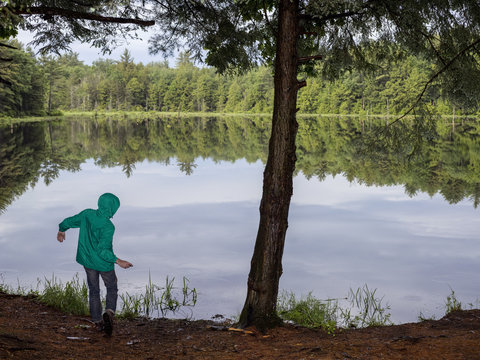 Person wearing waterproof jacket, skimming stones on lake, rear view