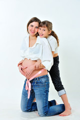 Pregnant mother and daughter embracing. They folded his hands on the bare stomach in the shape of a heart. Look at the camera and smiling. Portrait. Vertical view