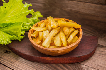 French fries on a wooden plate with greens. Close-up
