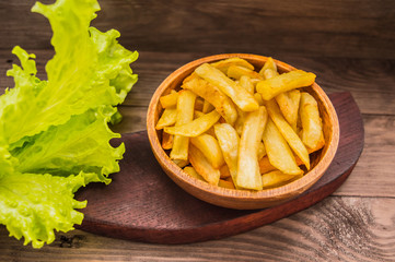 French fries on a wooden plate with greens. Close-up