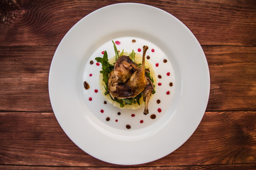 Roasted quail on a bed with mashed potatoes, rocket leaves and berry sauce.   white plate  wooden rustic background. Top view. Close-up